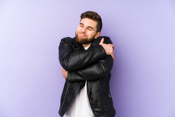 Young man isolated on purple background hugs, smiling carefree and happy. - Photo, Image