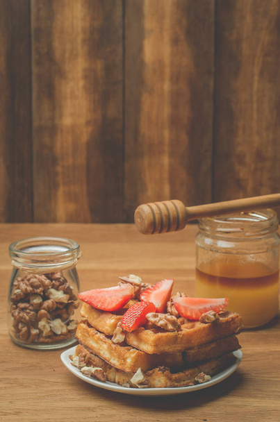 Tarro de miel con cazo de miel y las obleas caseras decoradas con fresa y nuez sobre un fondo de madera. Enfoque selectivo
 - Foto, imagen