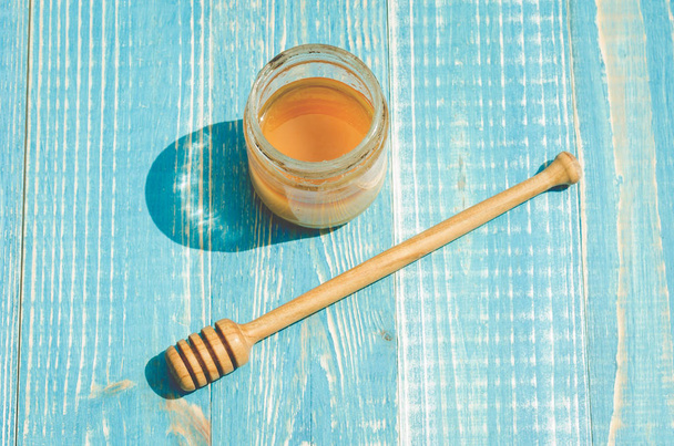 jar of honey and honey dipper on a blue wooden background, top view - Foto, Imagen