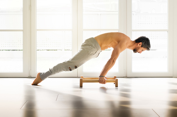 Muscular athletic man doing a calisthenics planche pose on low parallel floor bars in a bright spacious gym with copy space for a health and fitness concept - 写真・画像