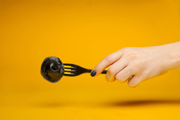 black dumpling on a black fork in a female hand on a yellow background - Fotoğraf, Görsel