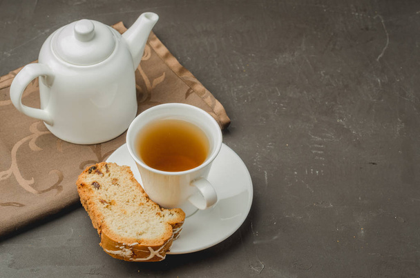  Breakfast with white tea cup and teapot with a pastries piece on dark stone table. Top view and copyspace - Photo, Image