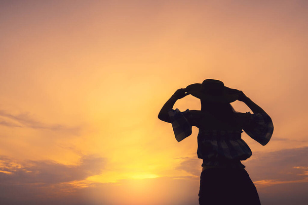 Silhouette von asiatischen Teenager-Frau Hand erheben Hut in den Himmel am Sonnenuntergang Strand Freiheit Ideen Konzept - Foto, Bild