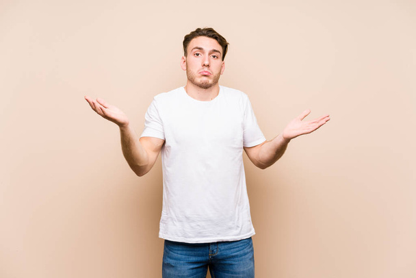 Young caucasian man posing isolated doubting and shrugging shoulders in questioning gesture. - Photo, Image
