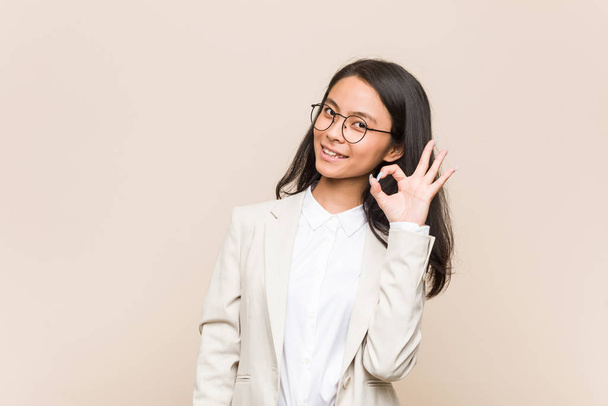 Giovane donna cinese business strizza l'occhio e tiene un gesto giusto con la mano
. - Foto, immagini