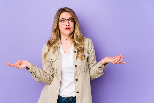 Young caucasian woman isolated on purple background doubting and shrugging shoulders in questioning gesture. - Photo, Image