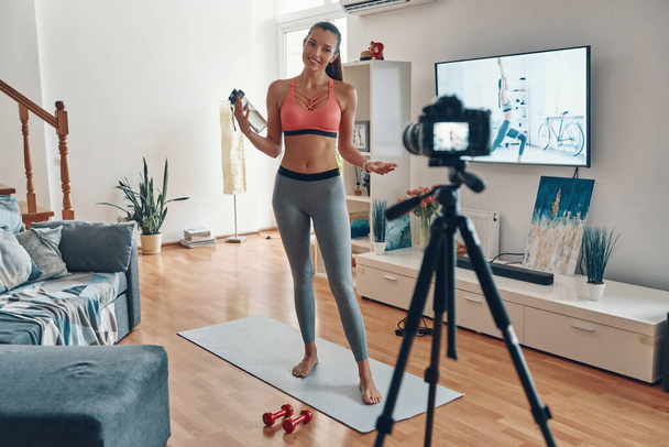 Full length of beautiful young woman in sports clothing working out and smiling while making social media video  - Φωτογραφία, εικόνα