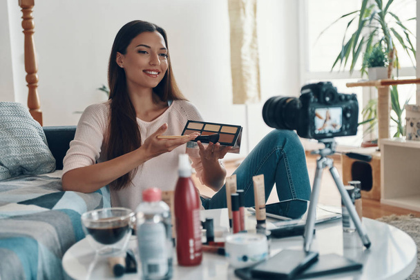 Confident young woman pointing at make-up palette and smiling while making social media video             - Фото, изображение