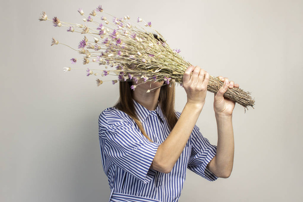 young girl holds a bouquet of wildflowers, a girl shows emotion on a light background. Banner. The concept of summer, vacation, travel, cosmetology. - Foto, imagen