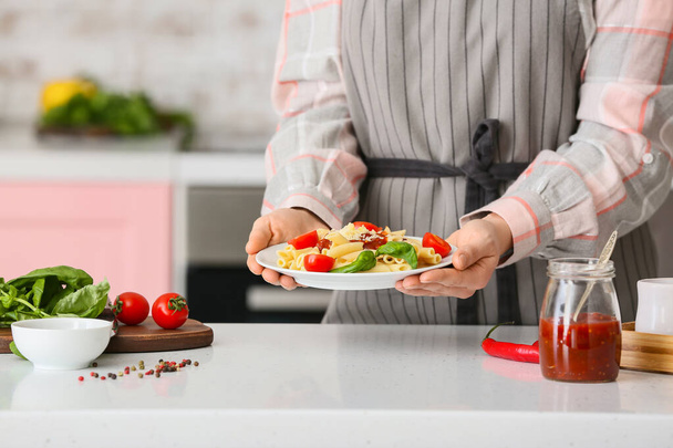 Mujer sosteniendo plato con pasta sabrosa en la cocina, primer plano
 - Foto, Imagen