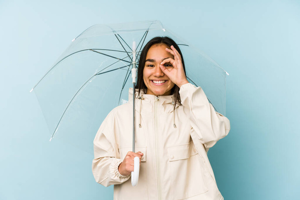 Joven asiática mujer sosteniendo un paraguas excitado mantener ok gesto en ojo
. - Foto, Imagen