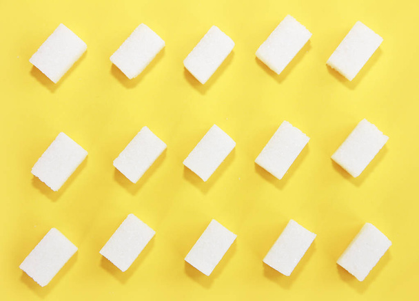 small pieces of natural white refined sugar on yellow background - Fotó, kép