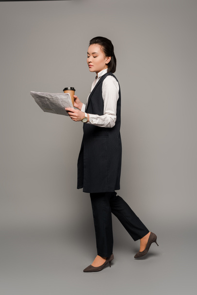 young businesswoman reading newspaper and drinking coffee on grey background - Zdjęcie, obraz