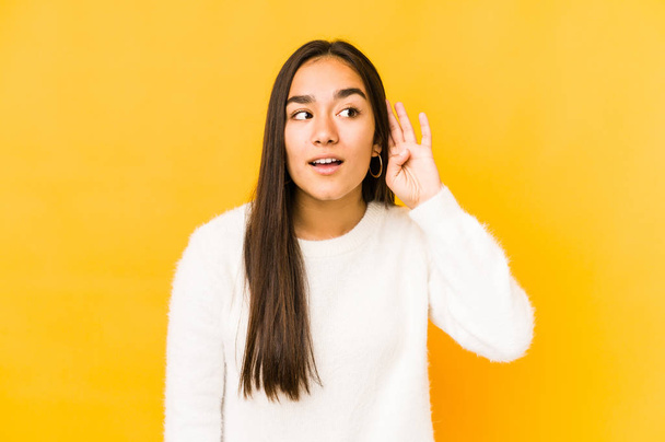 Young woman isolated on a yellow background trying to listening a gossip. - Photo, image