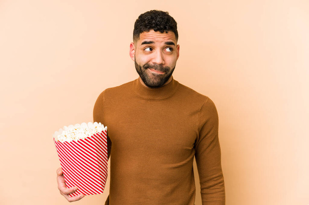 Young latin man holding a pop corn isolated confused, feels doubtful and unsure. - Foto, immagini
