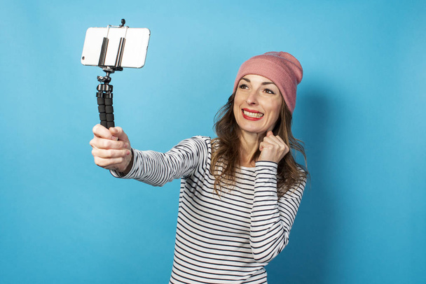 Young woman video blogger takes pictures of herself on the phone while broadcasting on a blue background. Concept story, vlog, selfie, blog. - Photo, Image