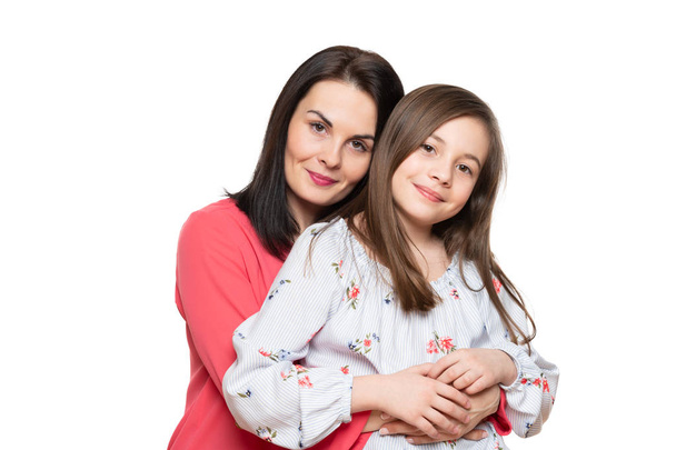 Waist up studio portrait of cute and playful schoolgirl embracing her mother. Happy smiling family background isolated over white background. - Fotó, kép