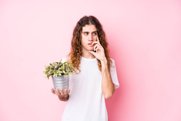Длинные волосы белый мужчина держит растение расслабленно думая о чем-то глядя на копировальное пространство
. - Фото, изображение
