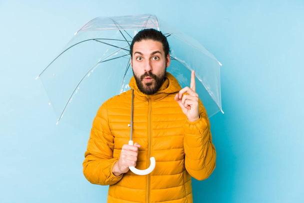 Молодий чоловік у довгому волоссі виглядає, тримаючи парасольку ізольованою, маючи якусь чудову ідею, концепцію творчості
. - Фото, зображення