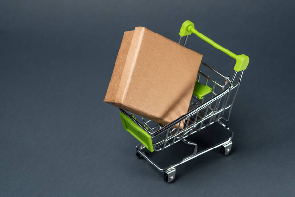 caja de cartón en un carro de compras de juguete sobre un fondo gris. Copiar espacio
 - Foto, Imagen