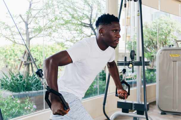 Muskularny Afroamerykański sportowiec wykonujący muchę kablową z urządzeniem treningowym stojącym przy oknie podczas treningu na siłowni - Zdjęcie, obraz