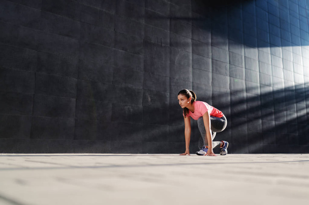 Beautiful fit caucasian brunette in sportswear kneeling and preparing to run. Back lit. - Foto, afbeelding