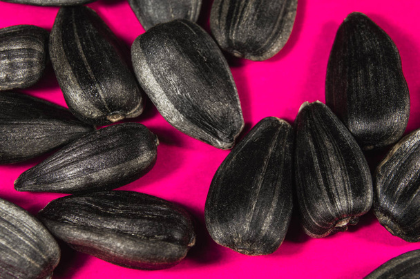 Black sunflower seeds in  macro isolated on pink background. Food photo with texture closeup. - Photo, Image