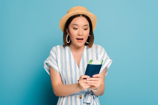 excitada chica asiática morena en vestido a rayas y sombrero de paja con pasaporte con tarjeta de embarque sobre fondo azul
 - Foto, Imagen