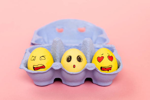 Foco seletivo de ovos de galinha pintados com expressões faciais em bandeja de ovos em fundo rosa, conceito de Páscoa
 - Foto, Imagem