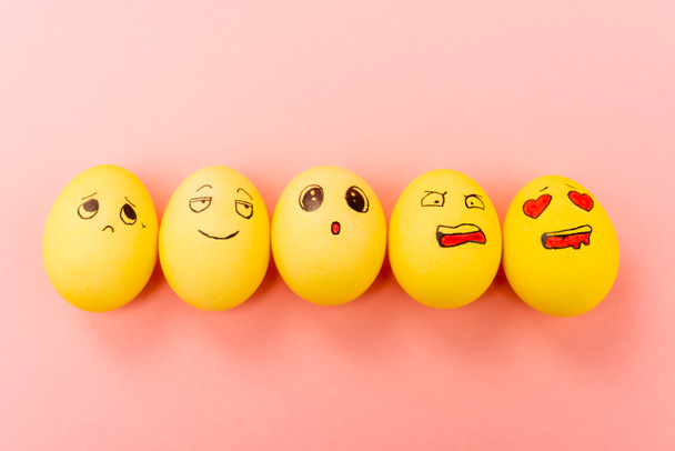 Vista superior de huevos de Pascua pintados con diferentes expresiones faciales sobre fondo rosa
 - Foto, imagen