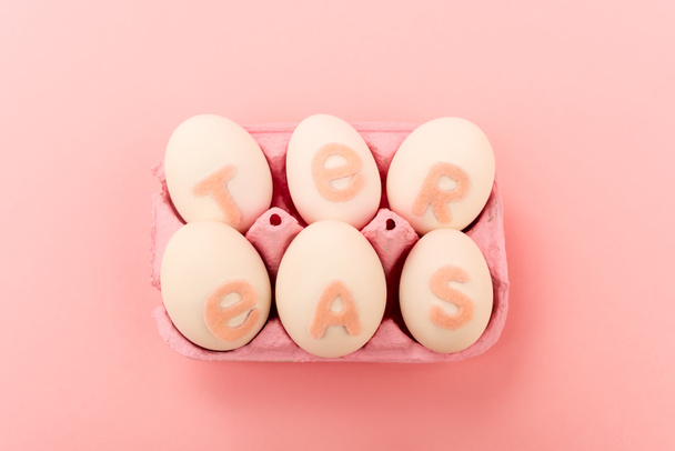 Άποψη υψηλής γωνίας των αυγών κοτόπουλου με πασχαλινά γράμματα στο δίσκο αυγών σε ροζ - Φωτογραφία, εικόνα
