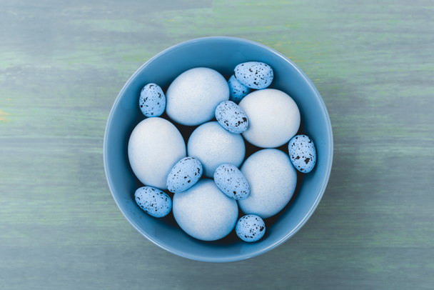 Top view of bowl with painted chicken and quail eggs on wooden background, easter concept - Foto, afbeelding