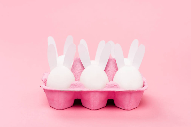 Conejitos decorativos de Pascua en bandeja de huevo sobre fondo rosa
 - Foto, Imagen