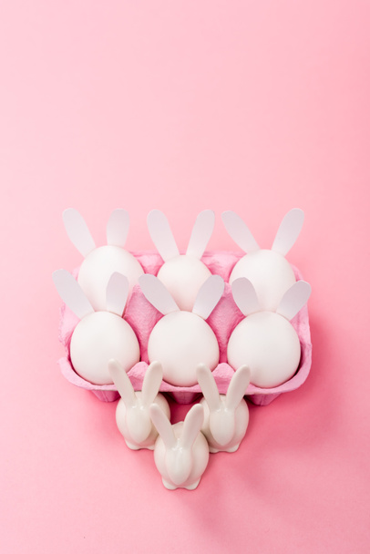 Vysoký úhel pohledu na dekorativní velikonoční králíky s vajíčkem zásobník na růžovém pozadí - Fotografie, Obrázek