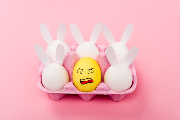 Süslü tavşanlar ve sarı yumurta pembe, paskalya konsepti üzerinde tahriş olmuş yüz ifadesi. - Fotoğraf, Görsel