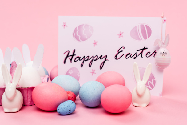Colorful eggs, decorative bunnies and card with happy easter lettering on pink background - Photo, Image