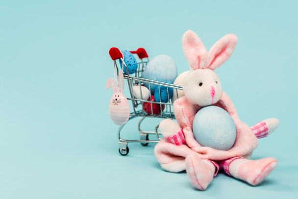 Renkli paskalya yumurtalı araba ve mavi arka planda dekoratif tavşanlar. - Fotoğraf, Görsel