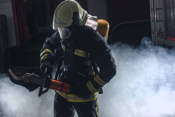 Porträt eines Feuerwehrmannes mit Drehleiter und Helm. Dunkler Hintergrund mit Rauch und blauem Licht. - Foto, Bild