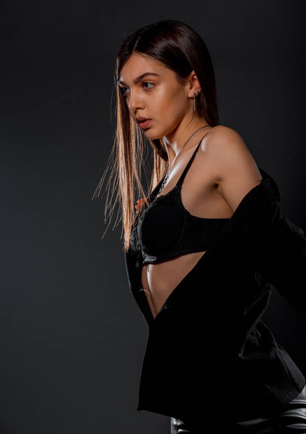 Portrait of a beautiful female model posing in trendy black top and leather pants - 写真・画像