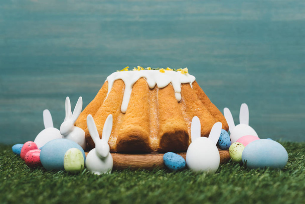Pan de Pascua con huevos coloridos y conejitos decorativos en la hierba
  - Foto, Imagen
