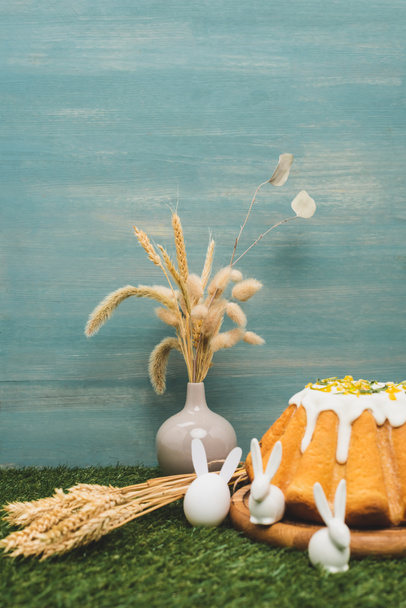 Bolo de Páscoa com coelhos decorativos e vaso com salgueiro e trigo na grama
 - Foto, Imagem