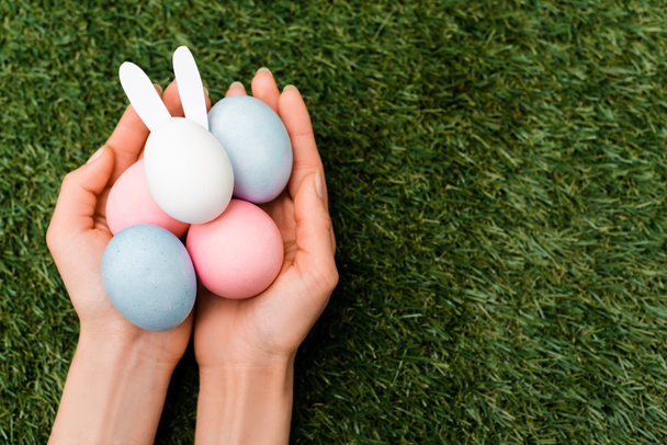 Cropped view of woman holding colorful chicken eggs and easter bunny on green background - Fotografie, Obrázek