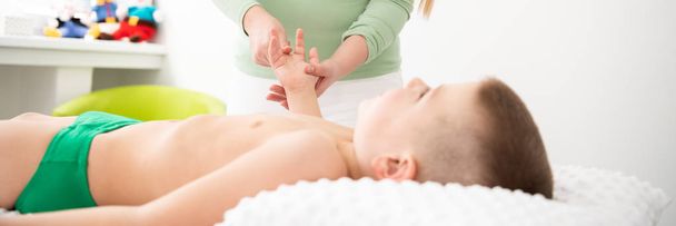 Kids massage concept web banner. Young female massage therapist giving a 6 year old boy arms massage. Physical therapy. - Foto, afbeelding