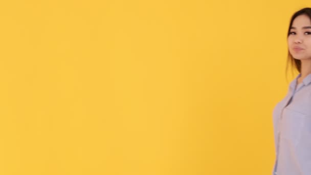 Young Asian girl on a yellow background waving at the camera. the woman welcomed - Filmmaterial, Video