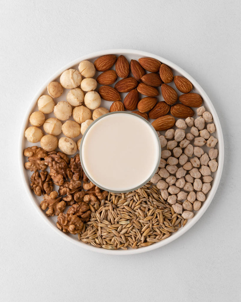 A set of macadamia nuts, walnuts, almonds, chickpeas, oats grains on a flat plate and glass cup with milk. - Photo, Image