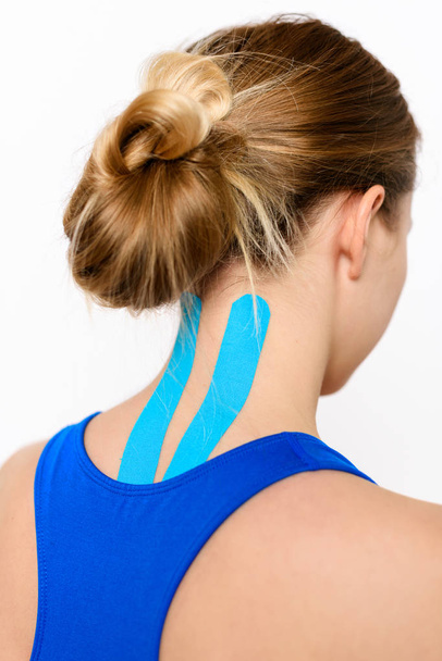 Rear view studio shot of a female patient with kinesio tape on her neck and back, isolated over white. Kinesiology, physical therapy, rehabilitation background. - 写真・画像