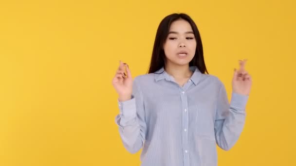 Asian young girl on a yellow background crossed my fingers in hope - Materiał filmowy, wideo