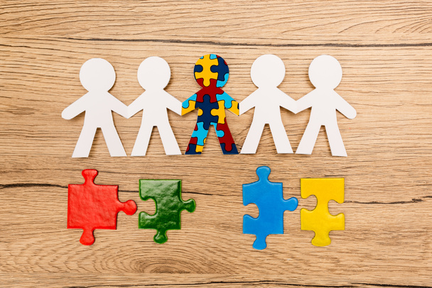 Top view of special kid with autism among another with colorful pieces of puzzle on wooden background - Photo, Image