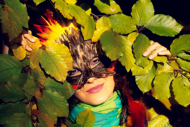 Νεαρή γυναίκα με πολύχρωμη μάσκα προσώπου από φτερά. - Φωτογραφία, εικόνα