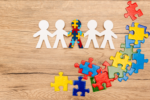 Top view of special kid with autism among another and pieces of bright colorful puzzle on wooden background - Photo, Image